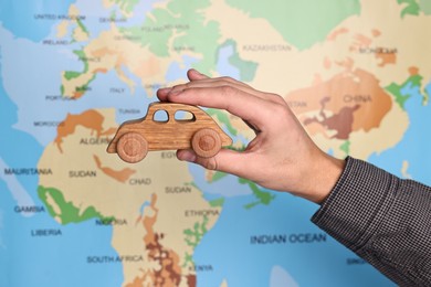 Photo of Woman holding wooden toy car against world map, closeup. Road trip