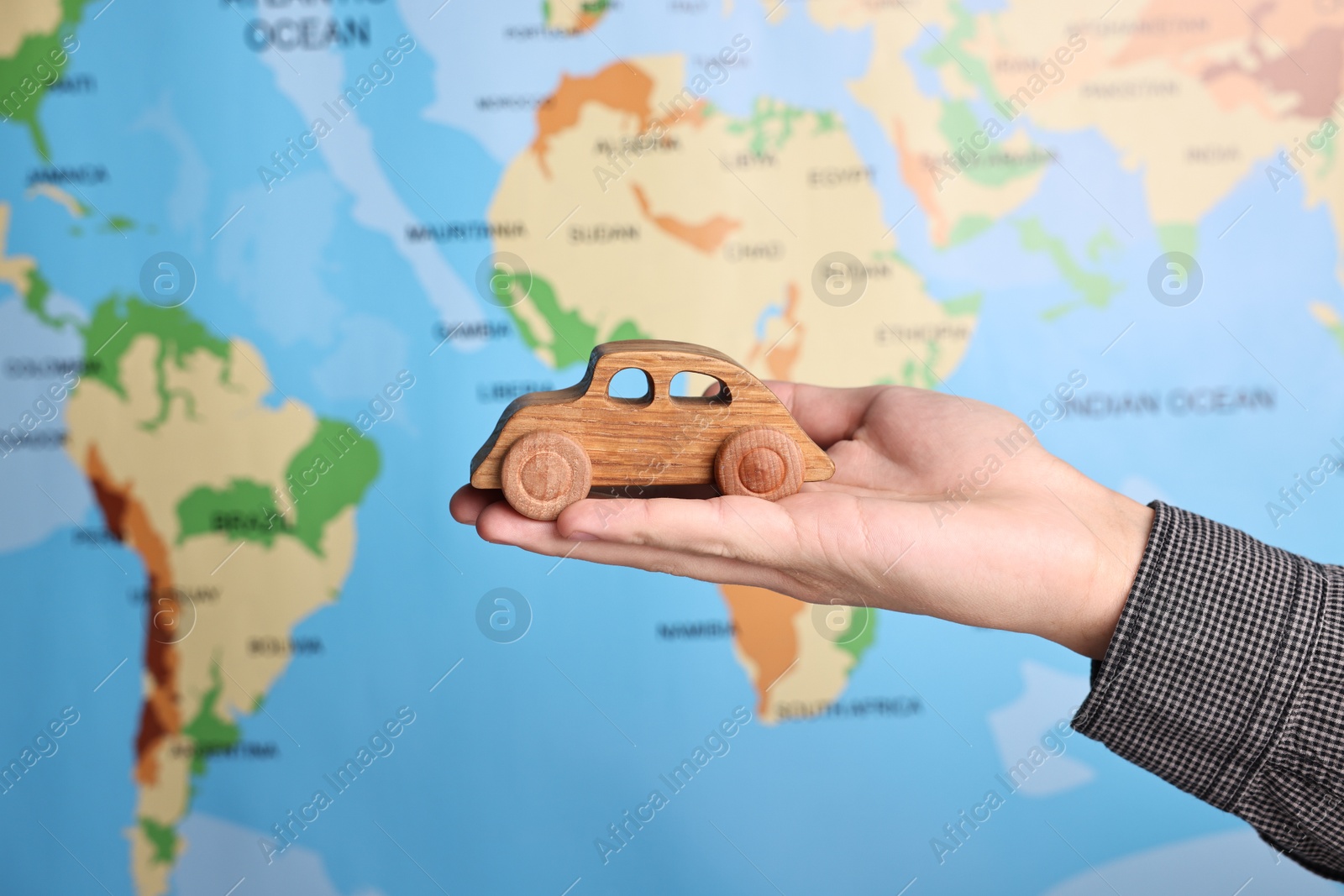 Photo of Woman holding wooden toy car against world map, closeup. Road trip