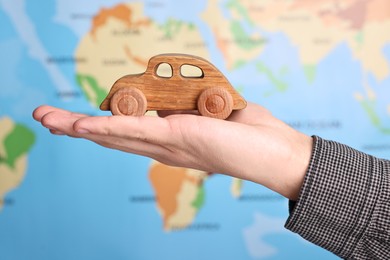 Photo of Woman holding wooden toy car against world map, closeup. Road trip