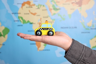 Photo of Woman holding yellow taxi car against world map, closeup. Road trip