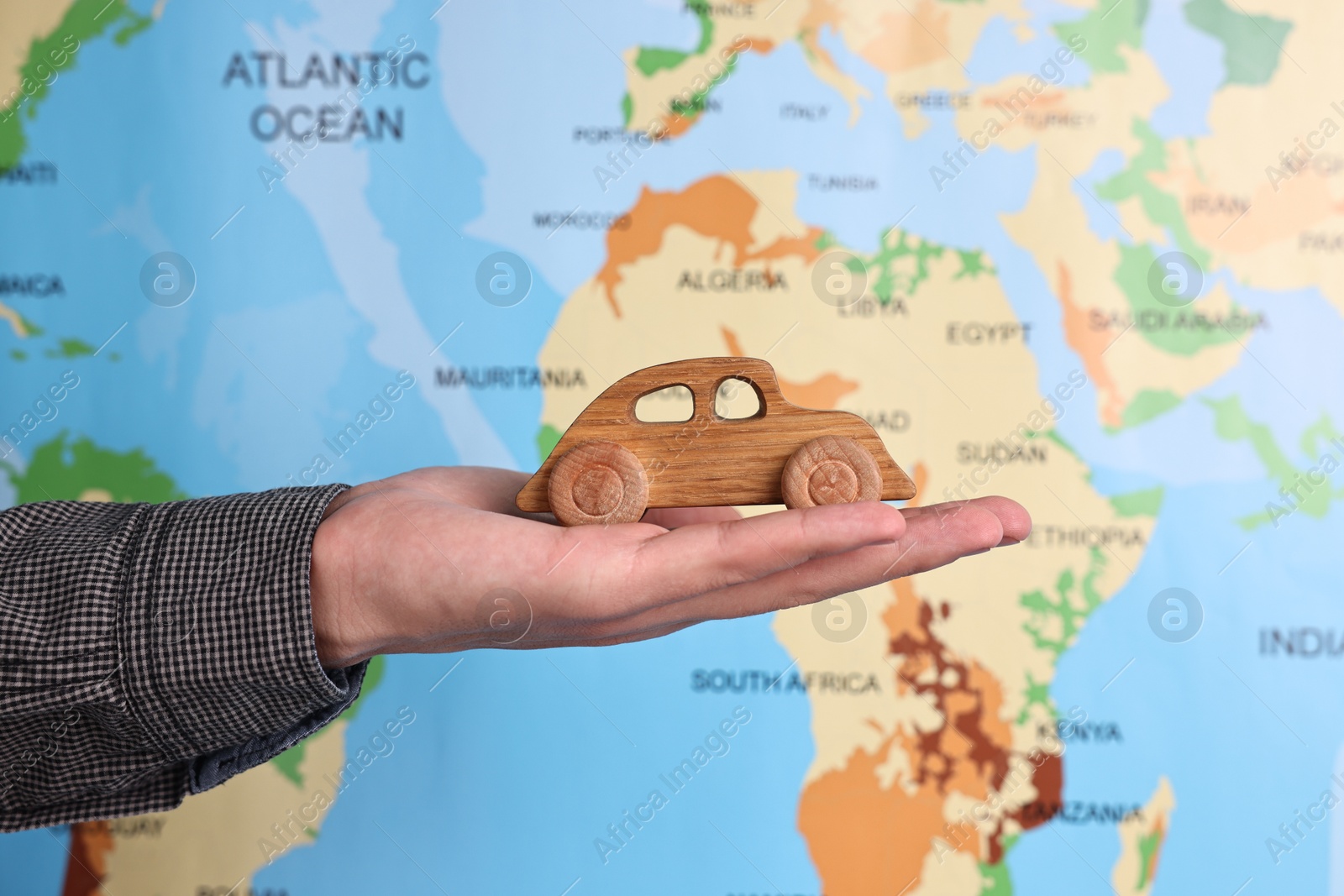 Photo of Woman holding wooden toy car against world map, closeup. Road trip