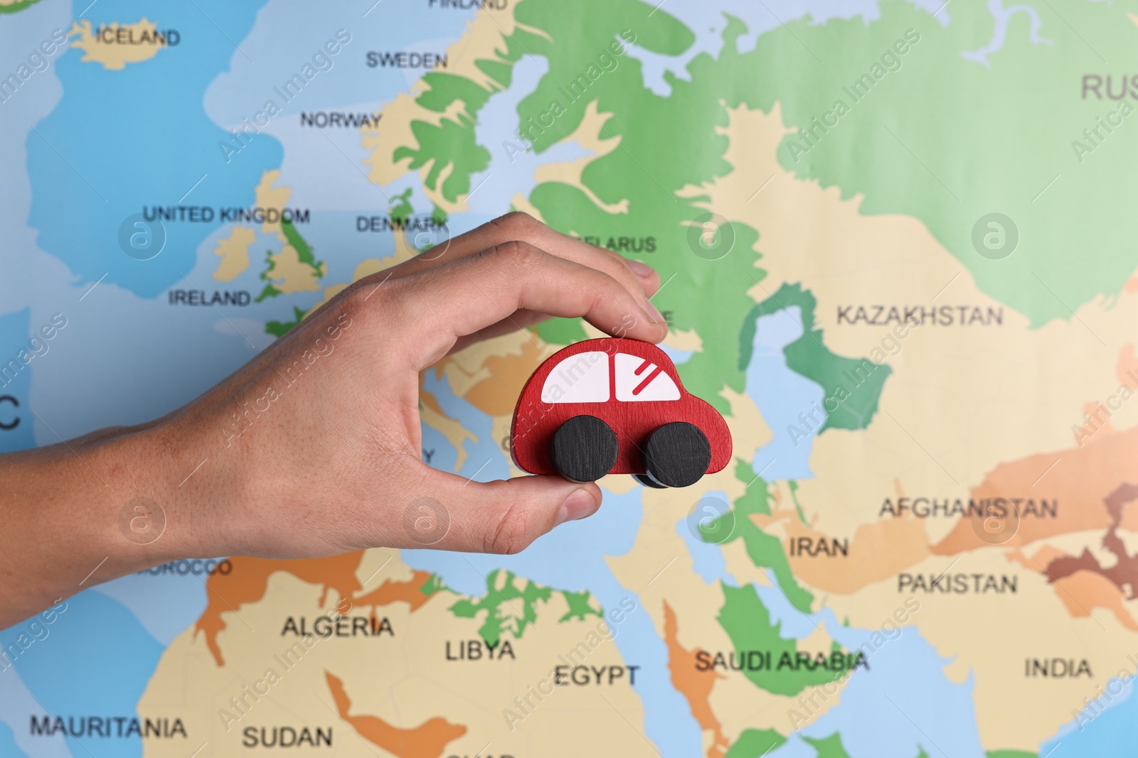 Photo of Woman holding red toy car against world map, closeup. Road trip