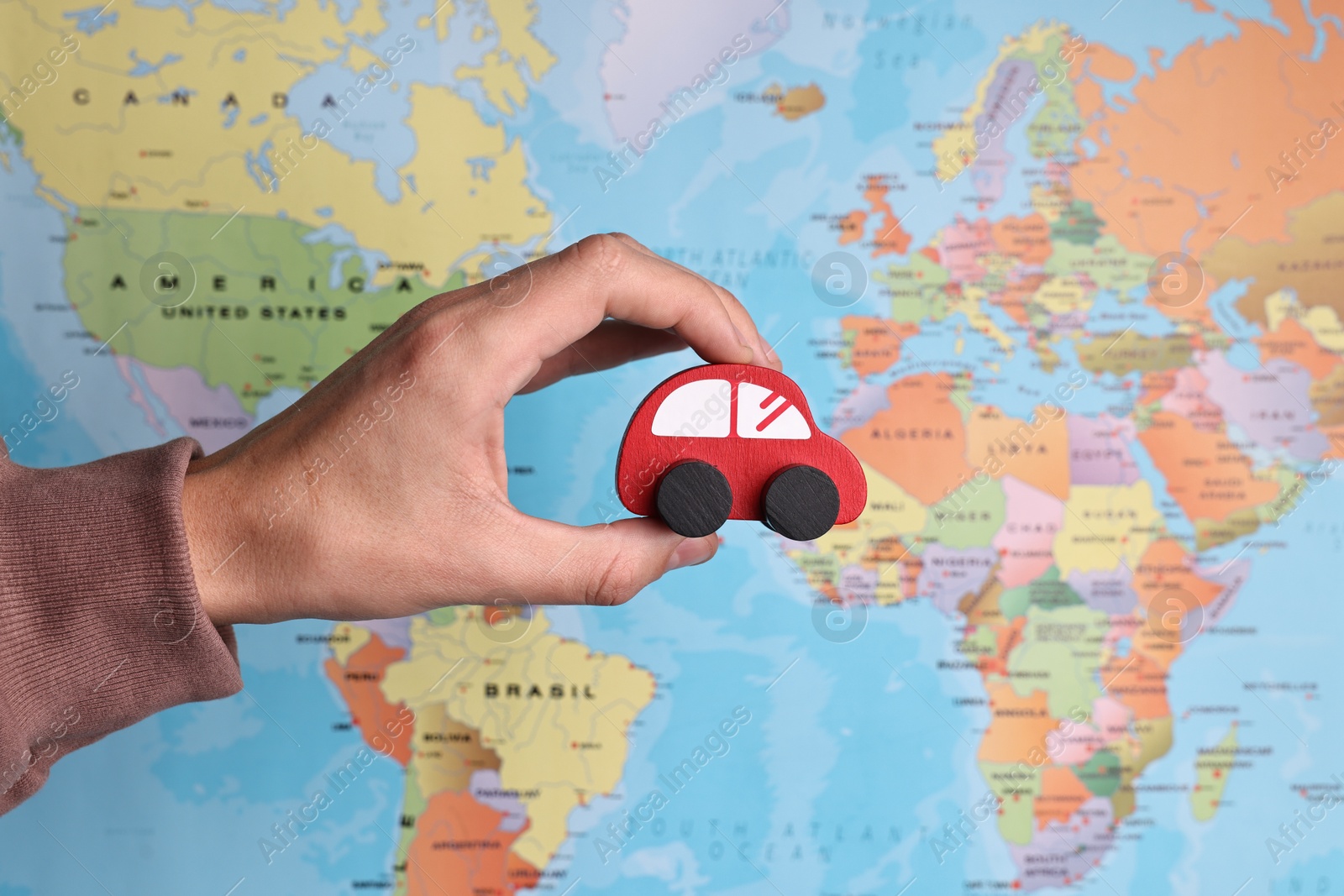 Photo of Woman holding red toy car against world map, closeup. Road trip