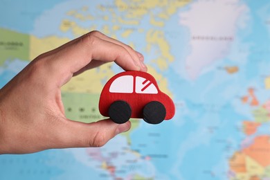 Photo of Woman holding red toy car against world map, closeup. Road trip