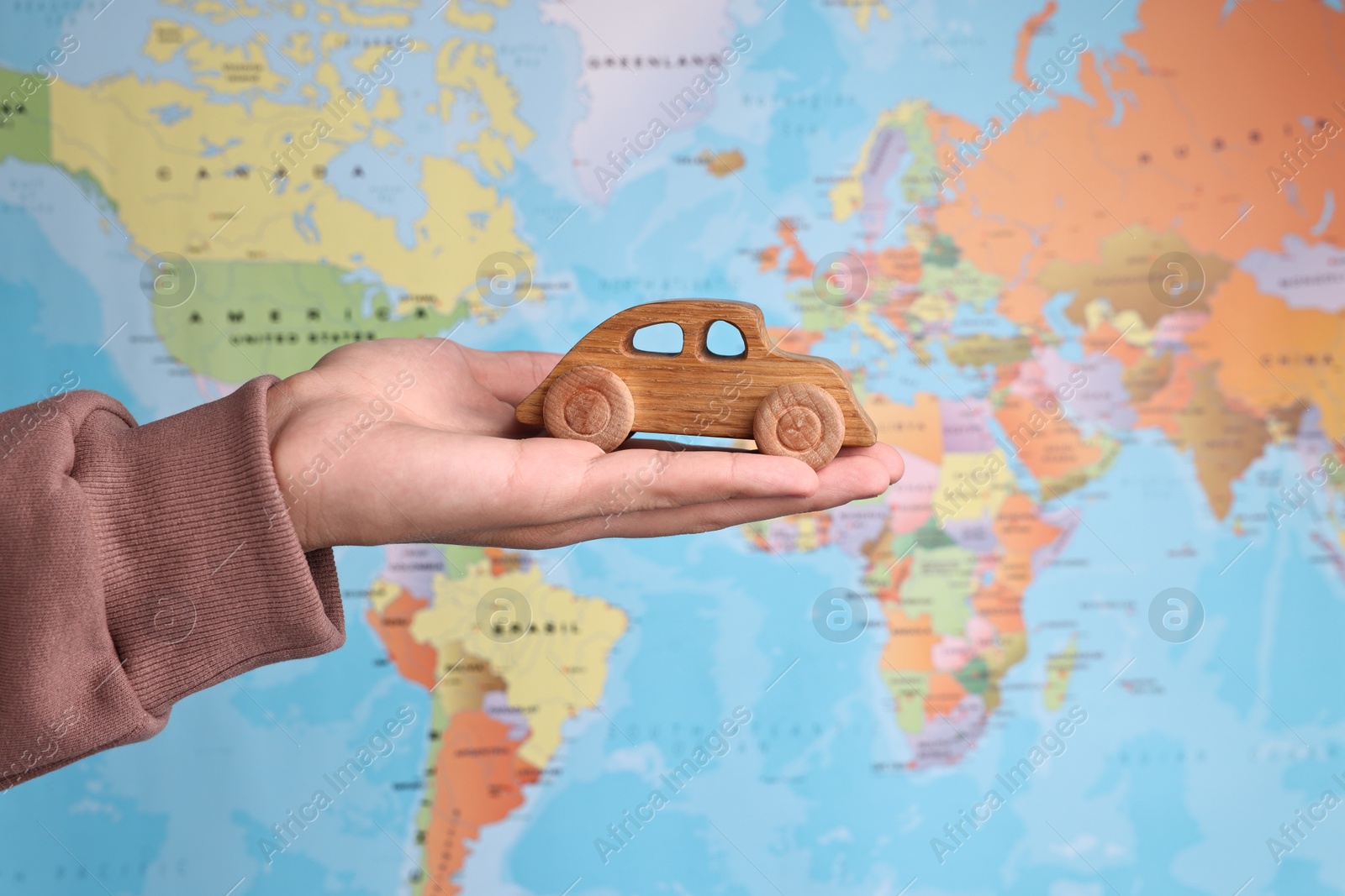 Photo of Woman holding wooden toy car against world map, closeup. Road trip