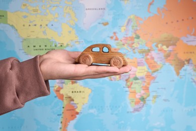 Photo of Woman holding wooden toy car against world map, closeup. Road trip