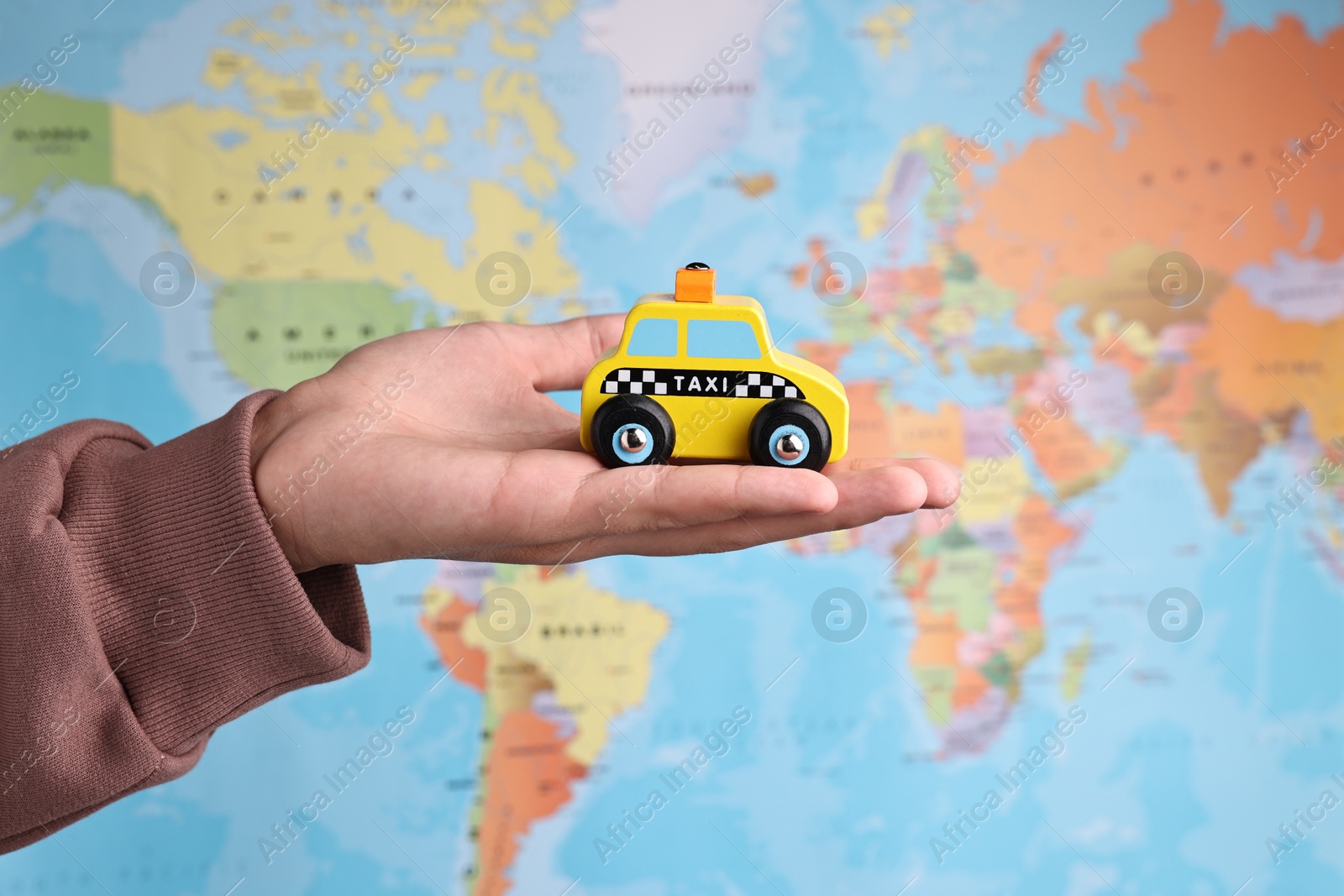 Photo of Woman holding yellow taxi car against world map, closeup. Road trip