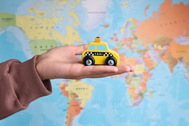 Photo of Woman holding yellow taxi car against world map, closeup. Road trip