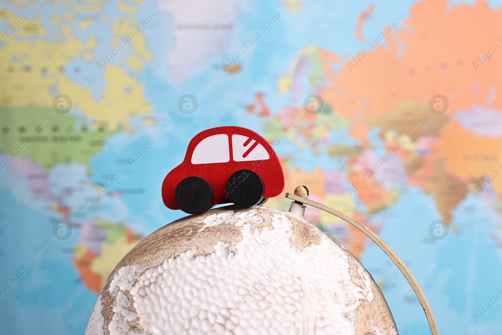 Photo of Red toy car on globe against world map, closeup. Road trip