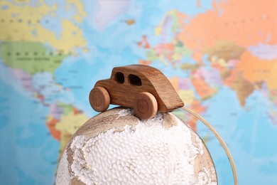 Photo of Wooden toy car on globe against world map, closeup. Road trip