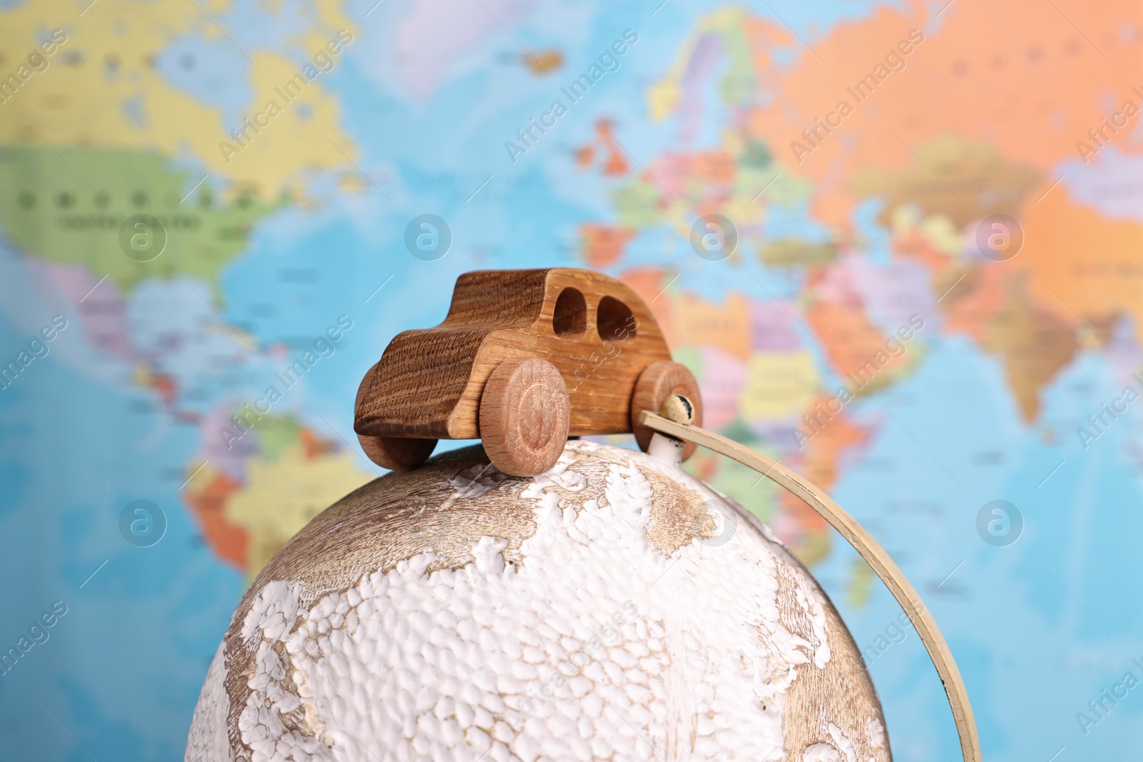 Photo of Wooden toy car on globe against world map, closeup. Road trip