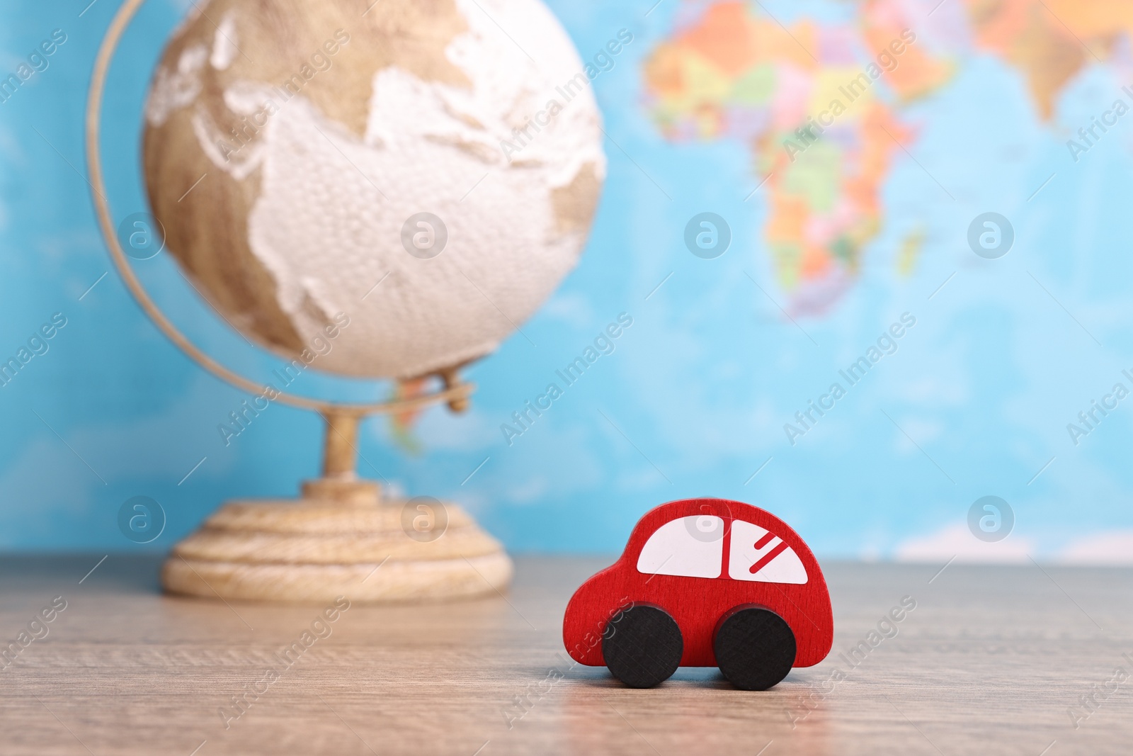 Photo of Red toy car and globe on wooden table against world map, closeup. Road trip