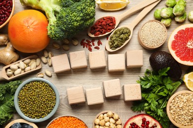 Photo of Different superfood products and blank cubes on wooden table, flat lay. Space for text