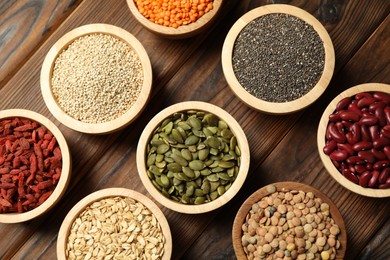 Photo of Different superfood products in bowls on wooden table, flat lay