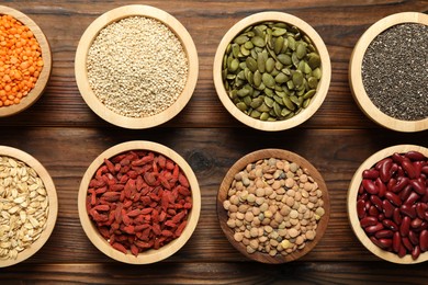 Photo of Different superfood products in bowls on wooden table, flat lay