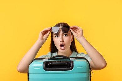 Photo of Emotional woman with suitcase wearing sunglasses on orange background