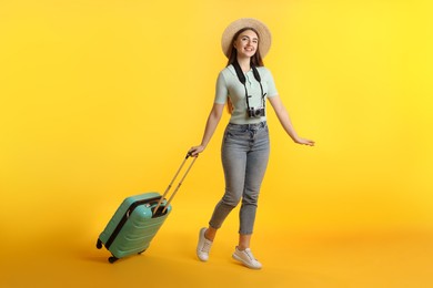 Photo of Happy woman with vintage camera and suitcase on orange background