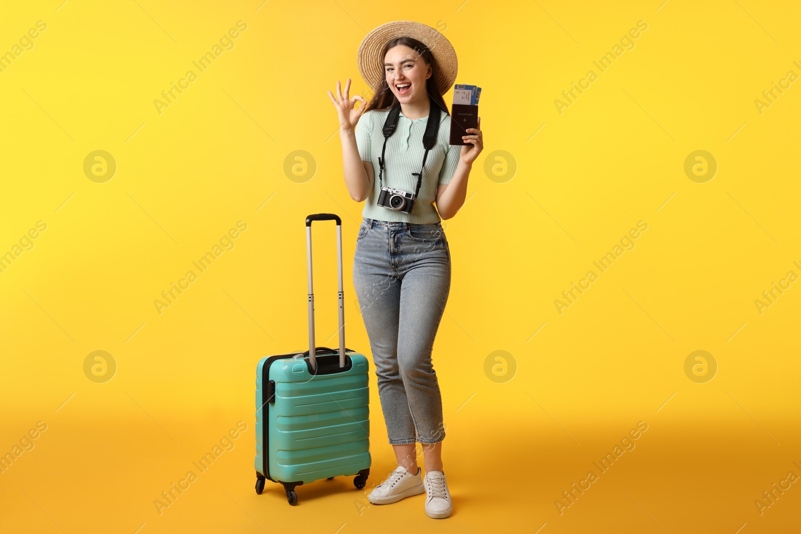 Photo of Woman with tickets, passport, suitcase and vintage camera showing ok gesture on orange background