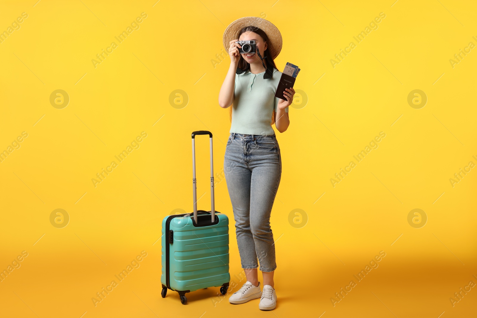 Photo of Woman with tickets, passport, suitcase and vintage camera on orange background