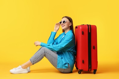 Photo of Woman with suitcase wearing sunglasses on orange background