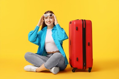 Photo of Woman with suitcase wearing sunglasses on orange background