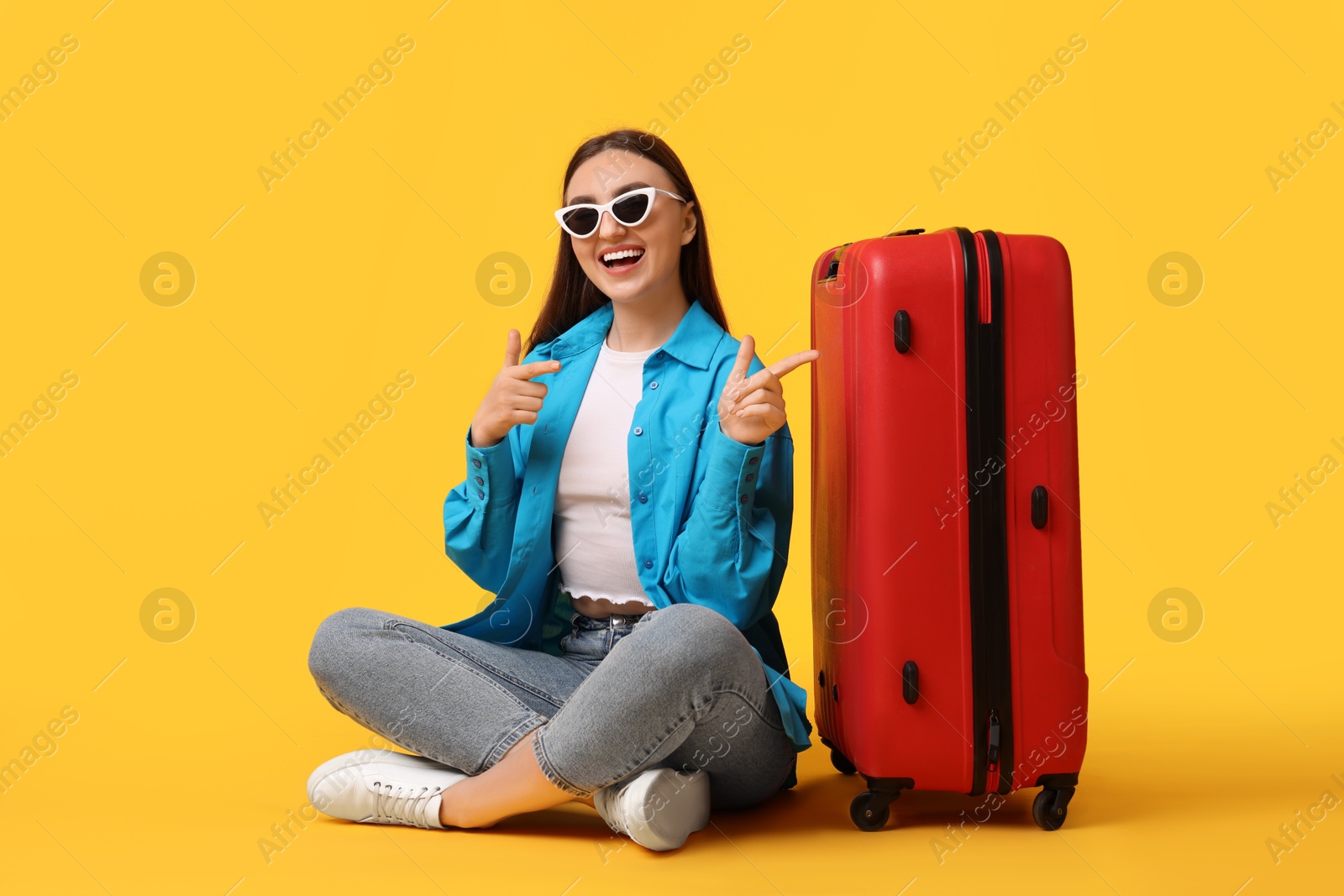 Photo of Woman with suitcase wearing sunglasses on orange background