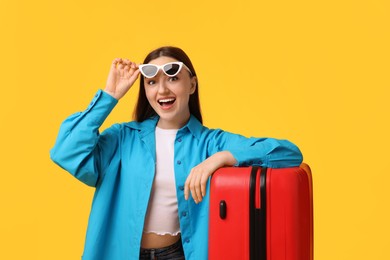 Photo of Woman with suitcase wearing sunglasses on orange background