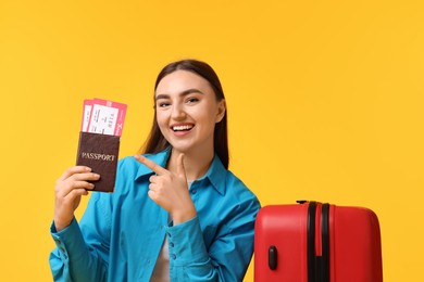 Photo of Woman with tickets, passport and suitcase on orange background