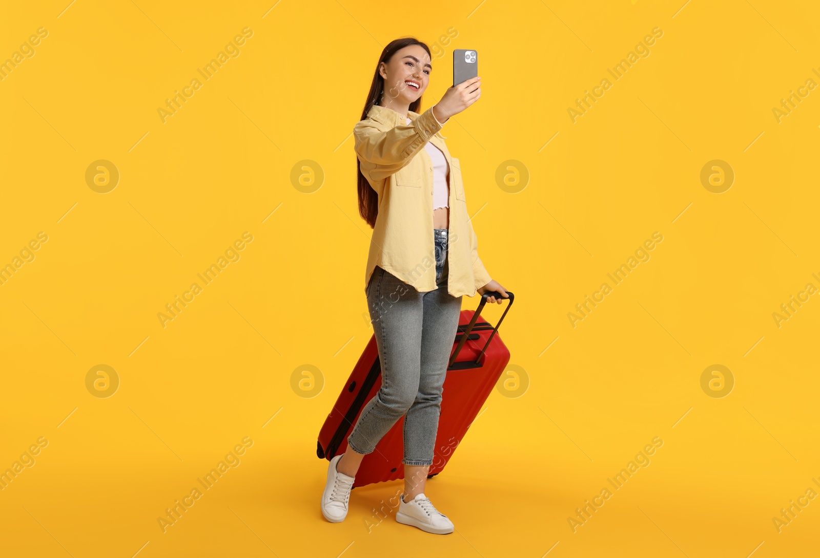 Photo of Happy woman with suitcase taking selfie on orange background