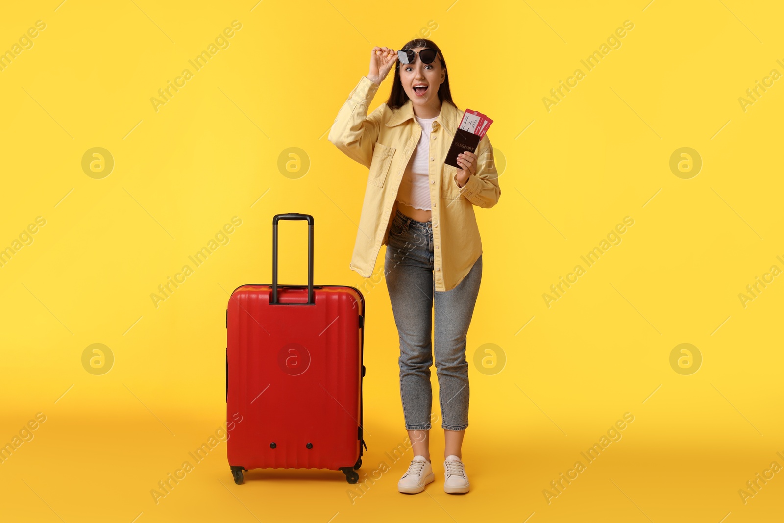 Photo of Woman with tickets, passport and suitcase on orange background