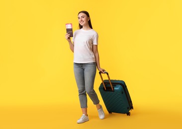 Photo of Woman with tickets, passport and suitcase on orange background