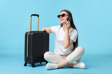 Photo of Woman with suitcase talking on smartphone against light blue background