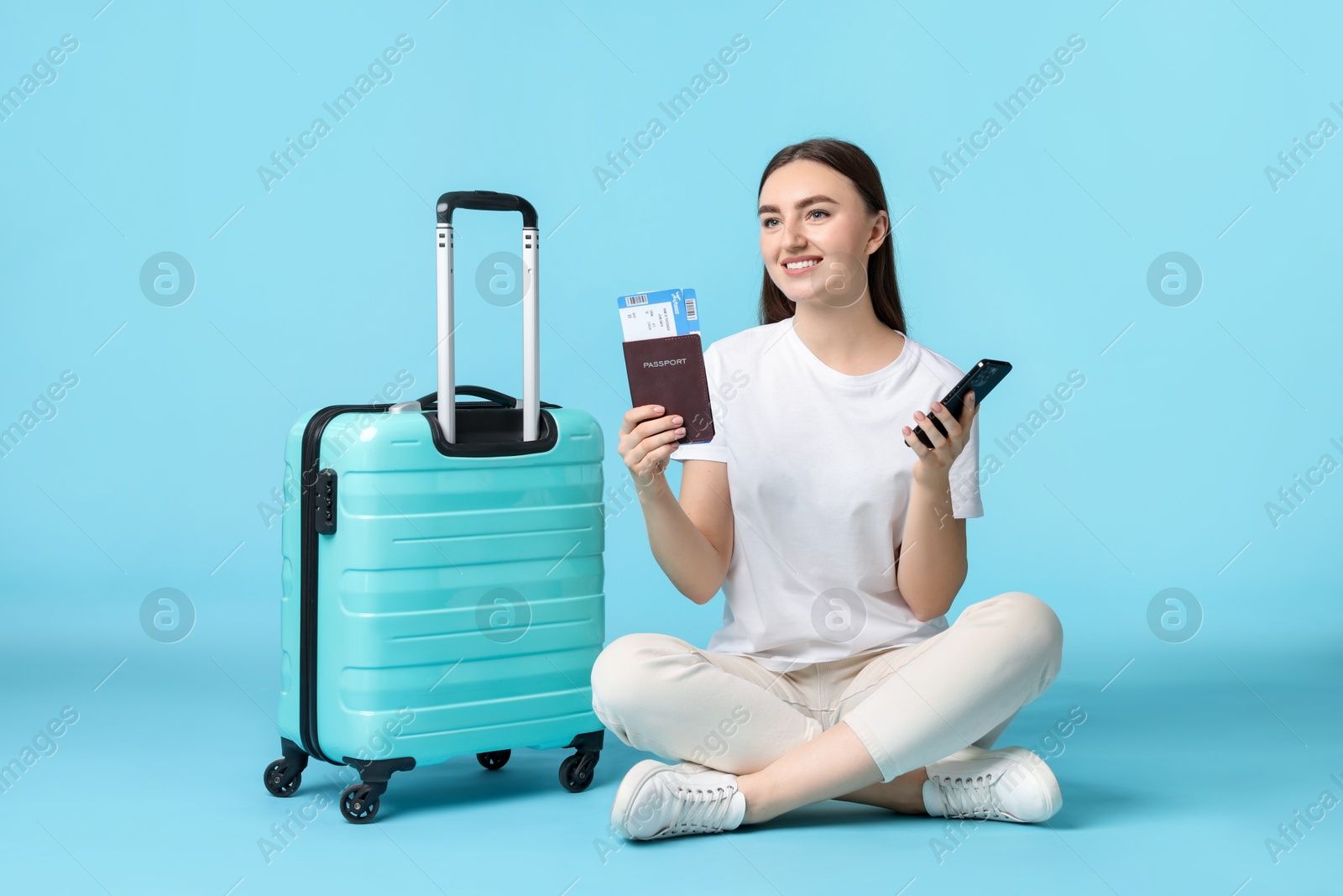 Photo of Woman with ticket, passport, suitcase and smartphone on light blue background