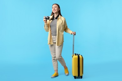 Photo of Woman with vintage camera and suitcase on light blue background