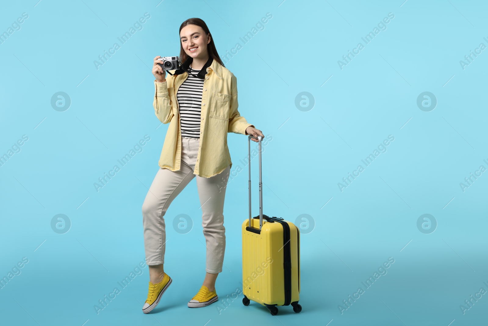 Photo of Woman with vintage camera and suitcase on light blue background