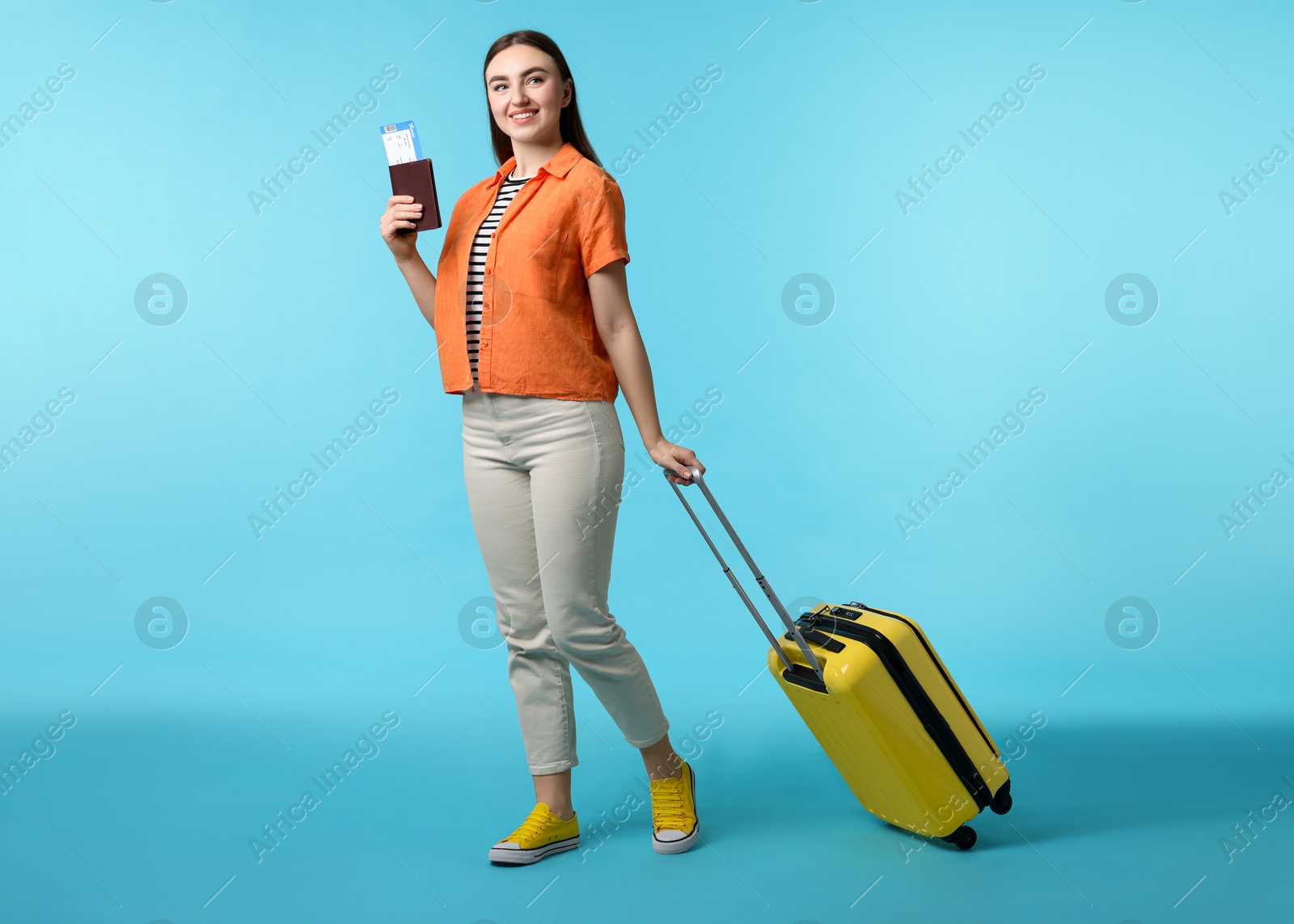 Photo of Woman with ticket, passport, and suitcase on light blue background