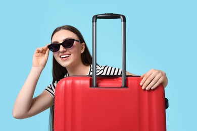 Photo of Woman with suitcase wearing sunglasses on light blue background