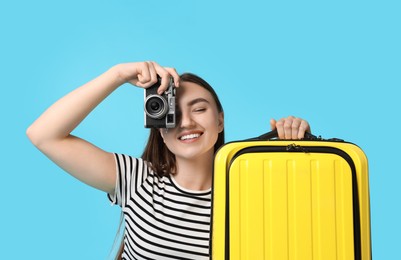 Woman with vintage camera and suitcase on light blue background