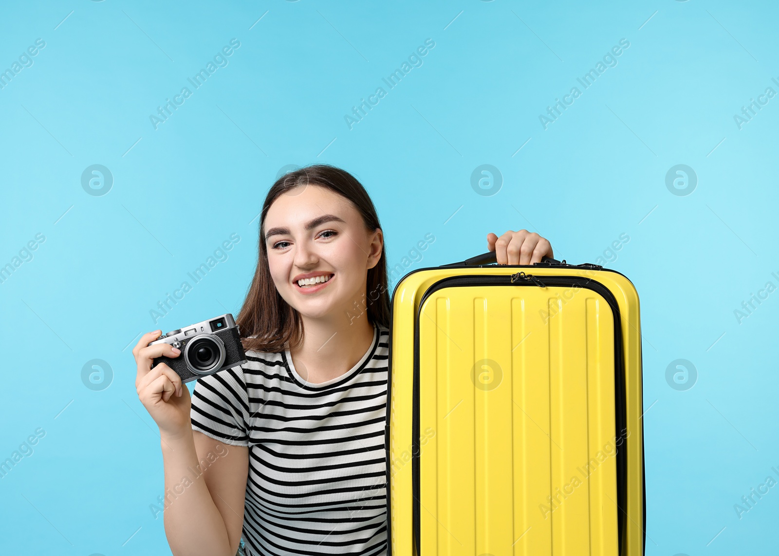 Photo of Woman with vintage camera and suitcase on light blue background