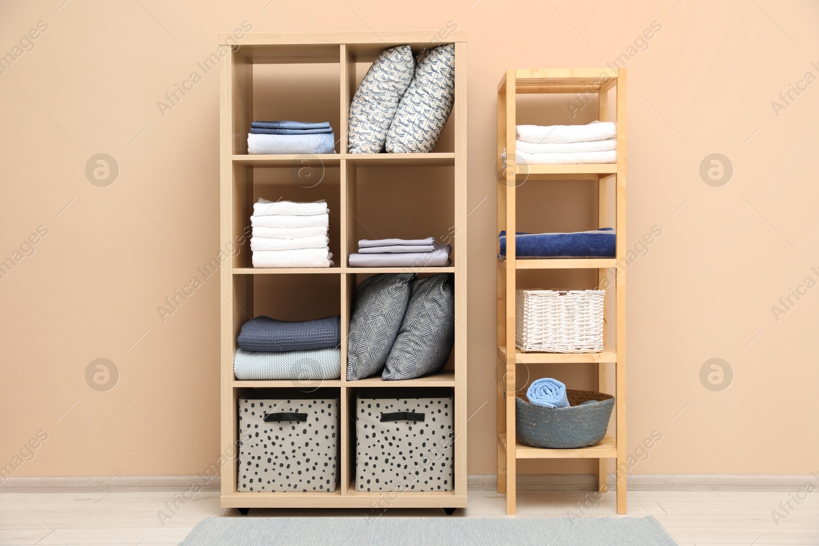 Photo of Home textile organization. Different pillows, linens towels and blankets on shelving units near beige wall