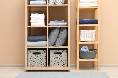 Photo of Home textile organization. Different pillows, linens towels and blankets on shelving units near beige wall