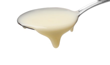 Photo of Delicious condensed milk pouring from spoon isolated on white