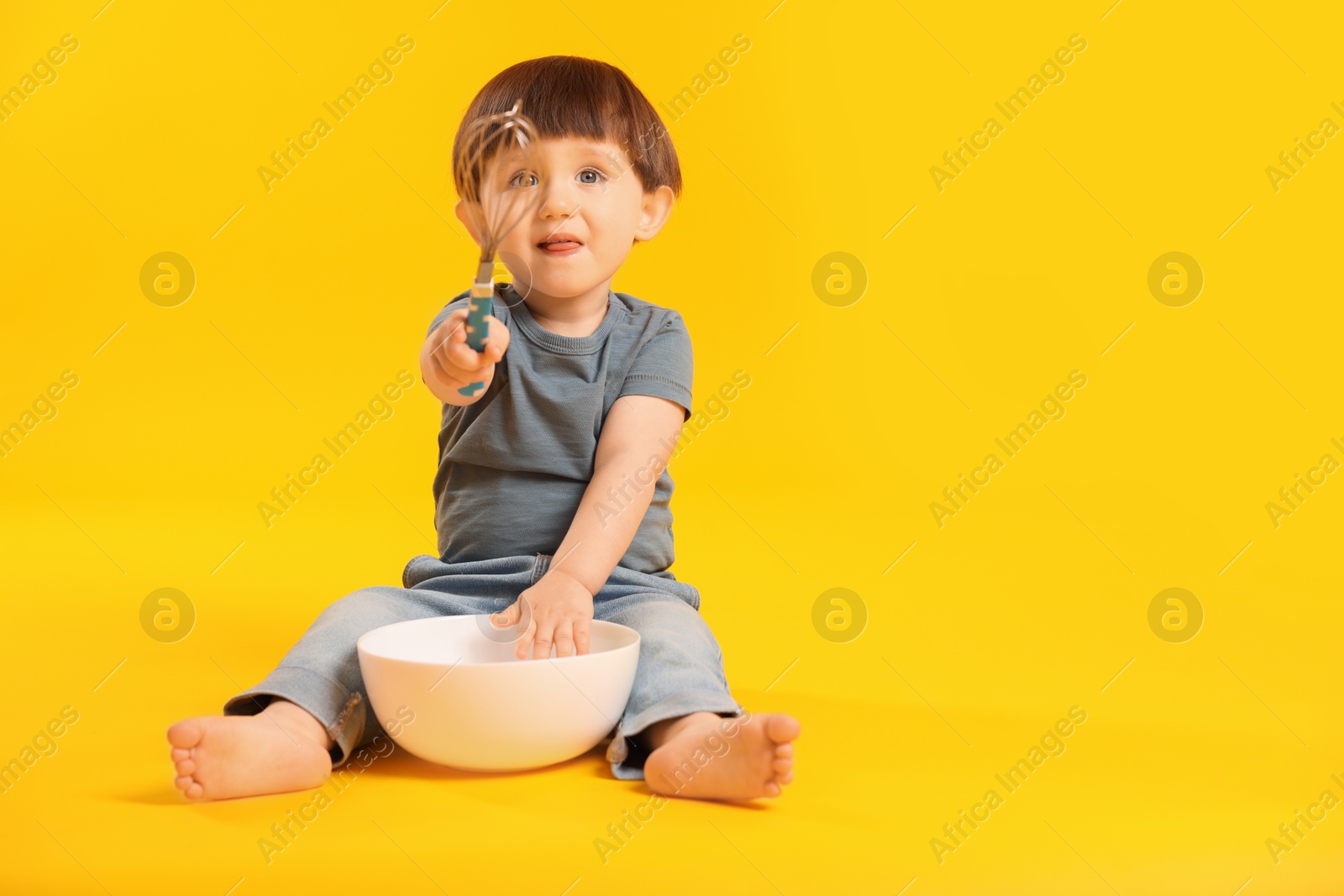 Photo of Cute little boy with bowl and whisk on yellow background. Space for text