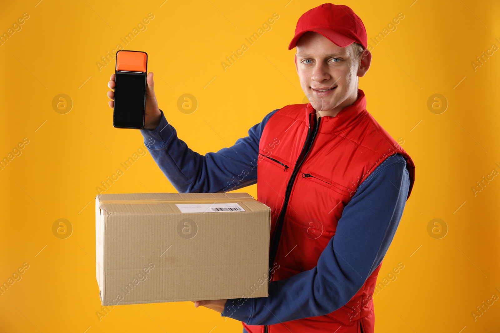 Photo of Happy courier with payment terminal and parcel on yellow background