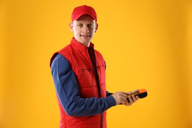 Photo of Happy courier with payment terminal on yellow background