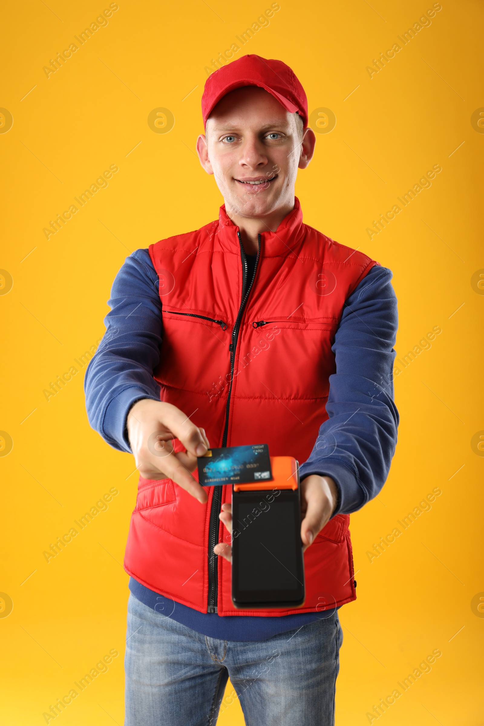 Photo of Happy courier with payment terminal and debit card on yellow background