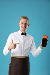 Photo of Happy waiter with payment terminal on light blue background