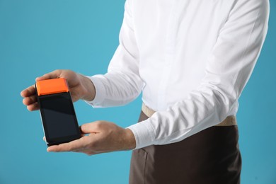 Photo of Waiter with payment terminal on light blue background, closeup