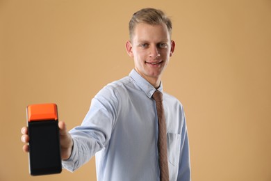 Photo of Happy young man with payment terminal on beige background