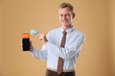 Happy young man with payment terminal on beige background